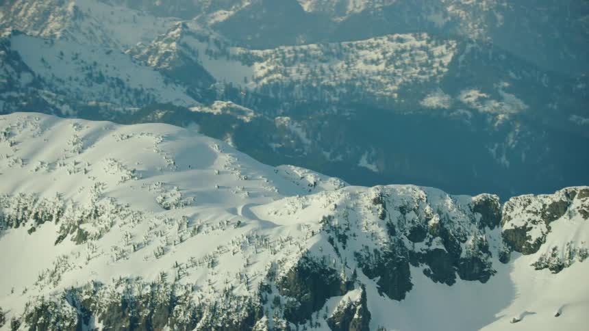 Wide shot of a small single engine airplane turning and climbing above glaciated and snow covered mountains in the winter