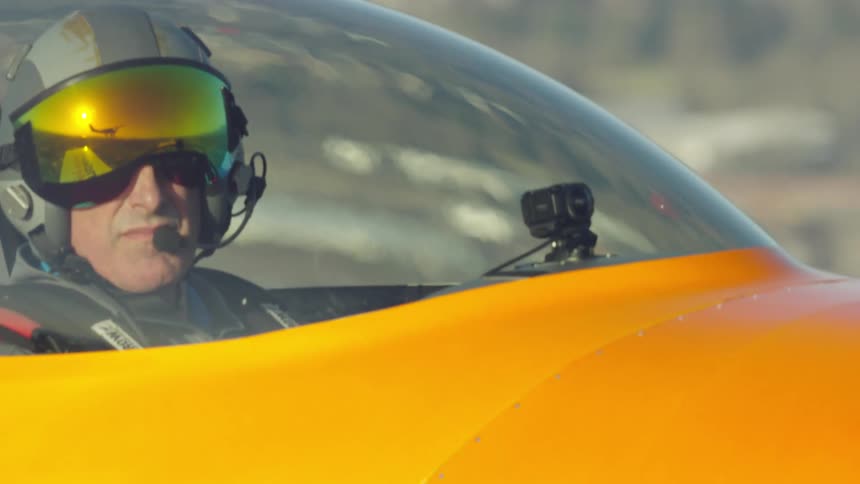 Pilot wearing a helmet sitting in a cockpit of an aricraft looking at the camera while flying just after takeoff