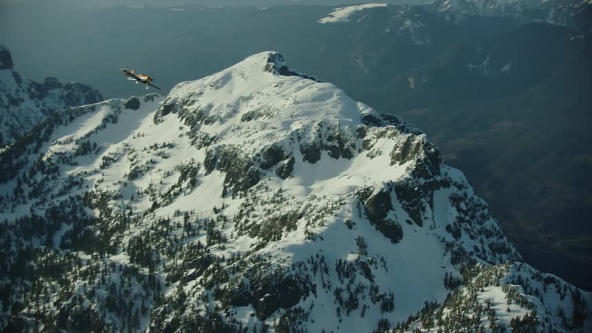 Airplane flies over snow covered mountains turning and coming closer to the camera in a cool formation shot