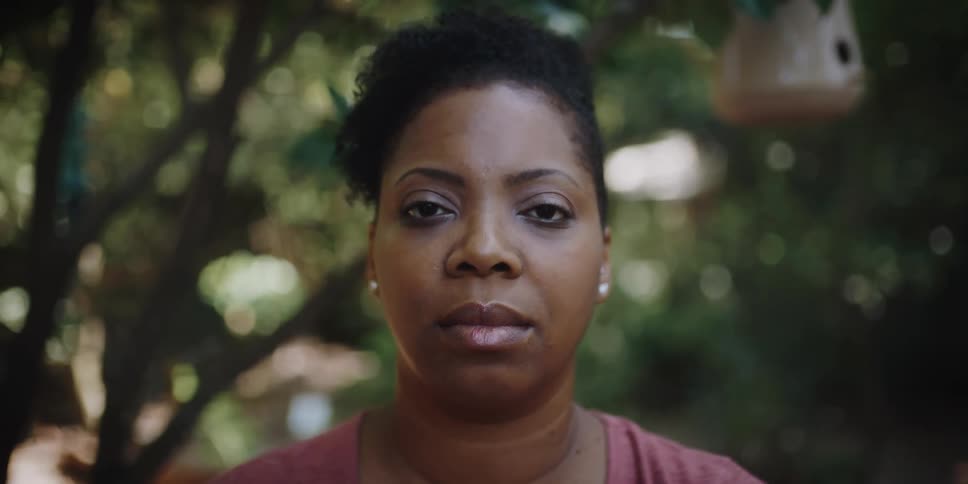 A woman standing under trees closes her eyes and then opens them