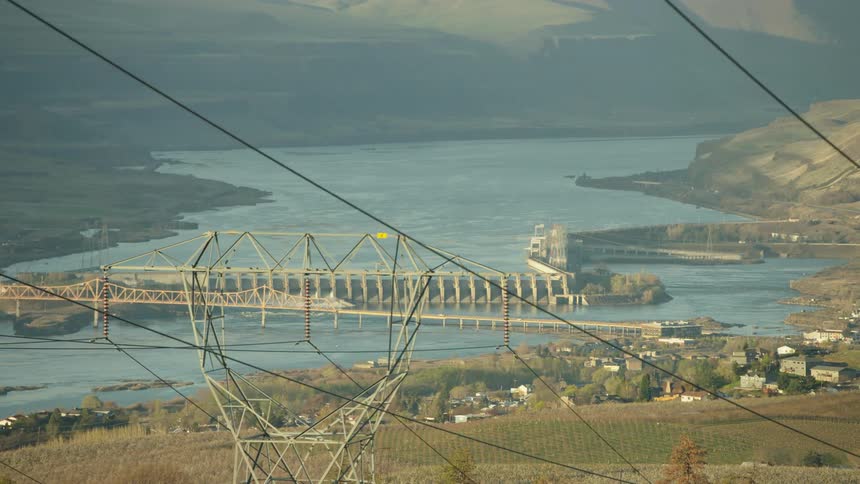 Large Electrical Transmission lines pass through the foreground with The Dalles Hydroelectric dam in the background communicating the energy consumption needs of the world
