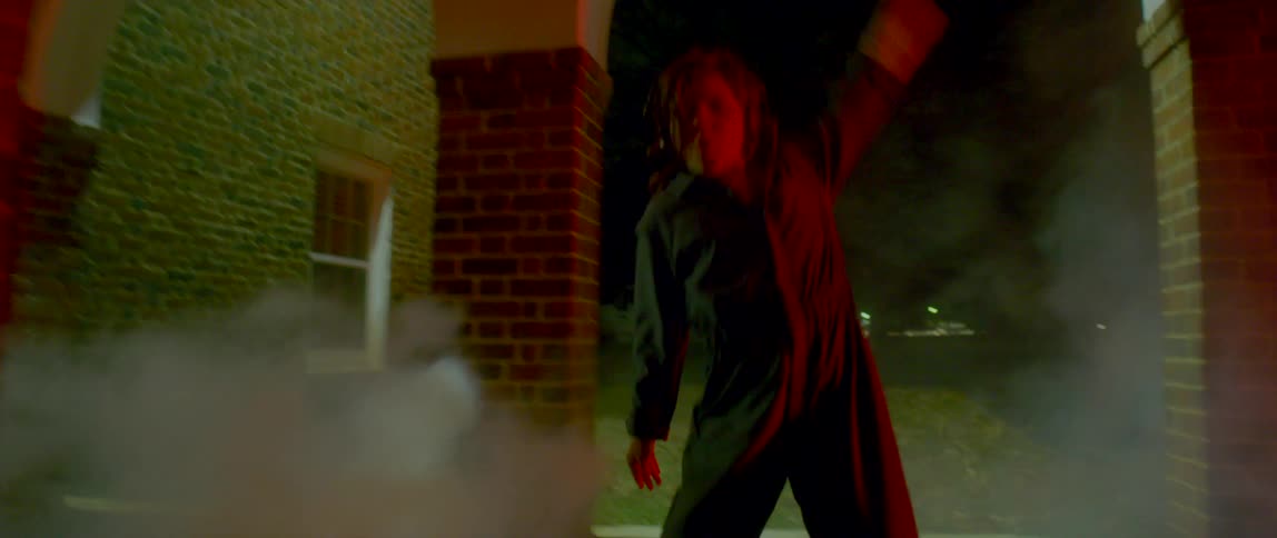 Girl wearing overalls dancing outside a building at night surrounded by white smoke