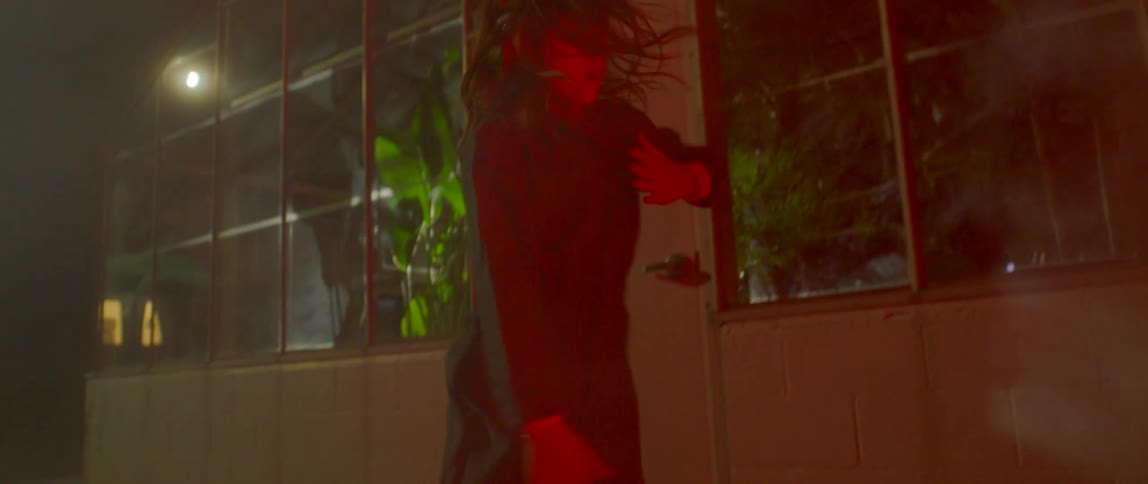 Girl wearing overalls dancing outside a building at night surrounded by smoke