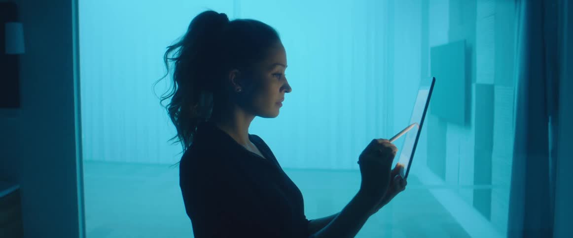 A woman in a room using a tablet with a stylus with a wall in the background