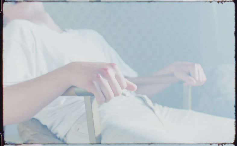A teenager sits in a chair with his head back in front of flashing television