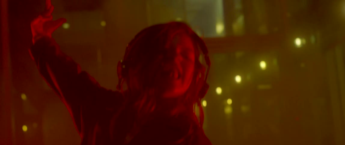 A woman performs a spin and starts dancing wildly in a room with fog and a flashing red light