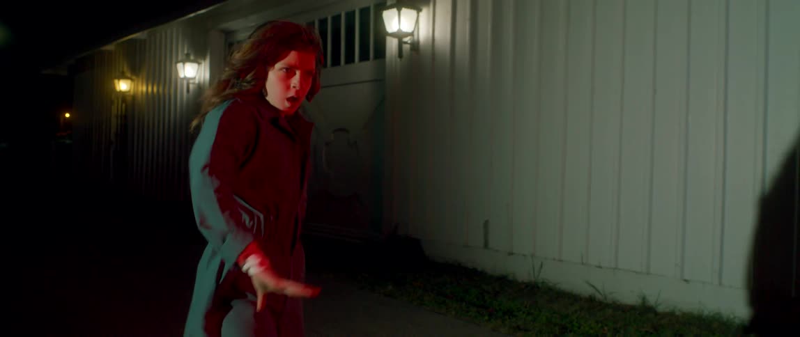 A woman pops and locks while dancing outside her house at night in a green jumpsuit