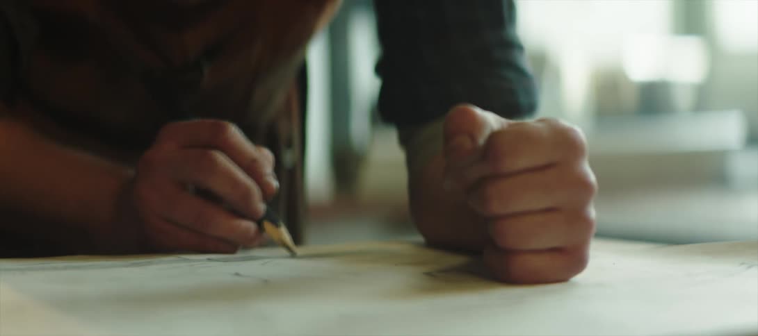 Man uses a pencil to draw on paper over the workbench on a workshop