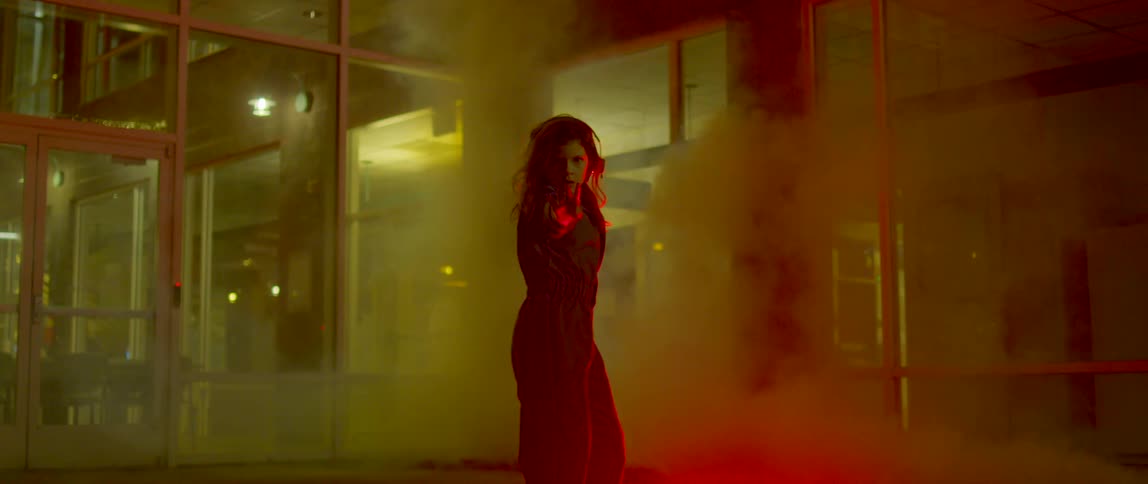 A woman dancing in fog while a white light flashes outdoors in front of a building