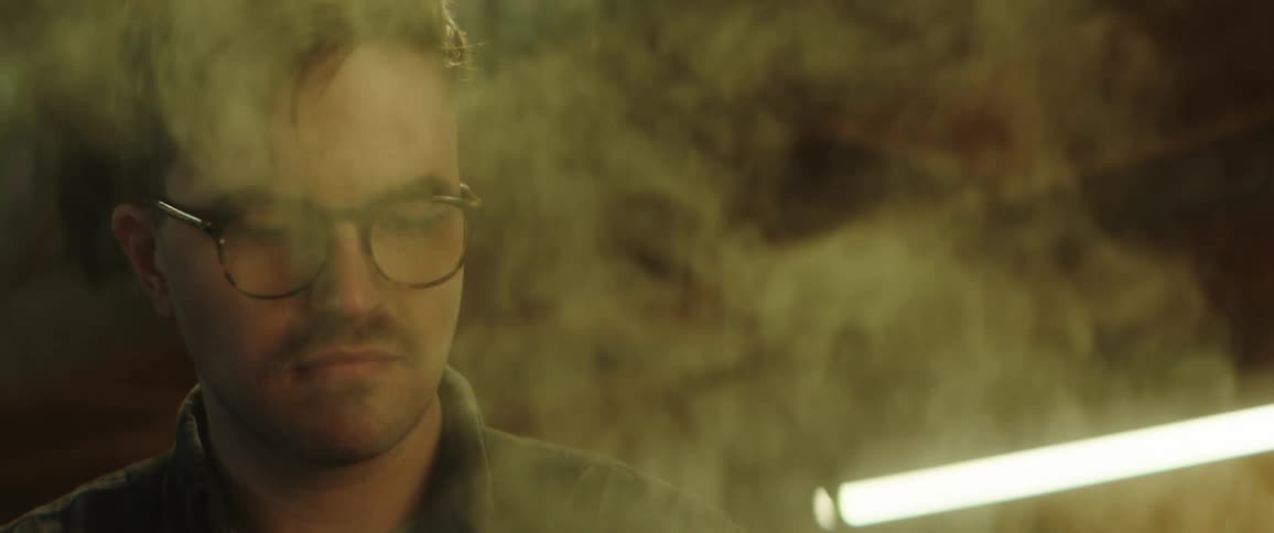 Steam blowing up into the face of a man with glasses inside of a room