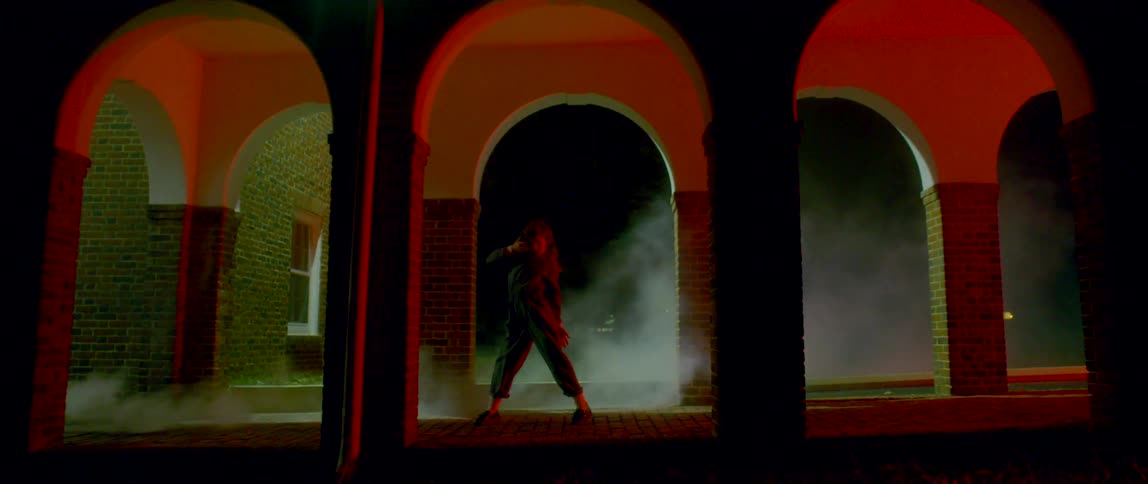 A woman dancing in a hallway with smoke with pillars and arches