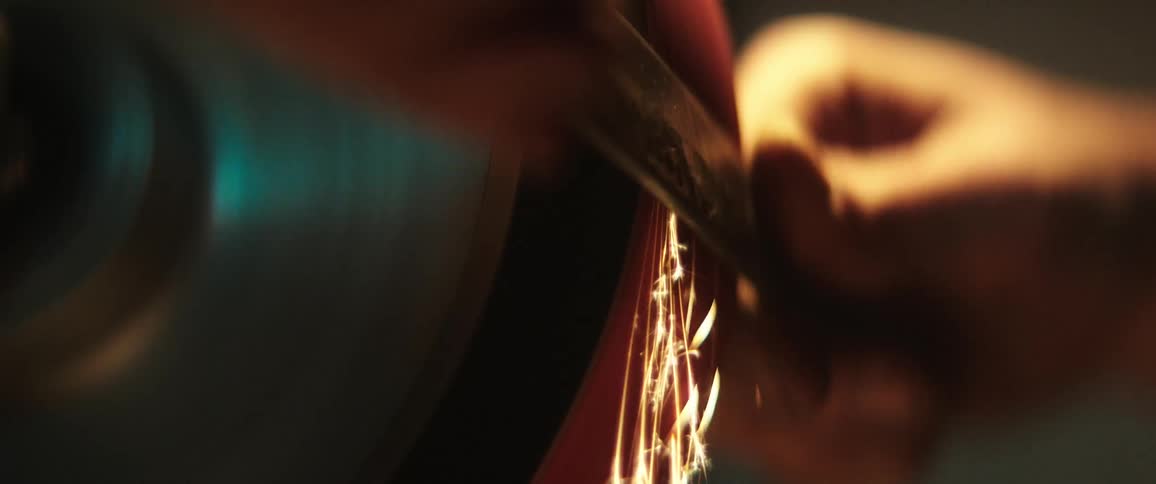 Sparks fly as a man holds a piece of metal against a spinning grinder