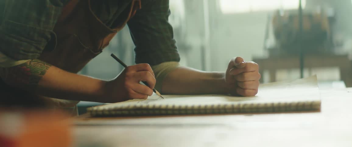 A person in a room with an apron drawing on a notepad on a table