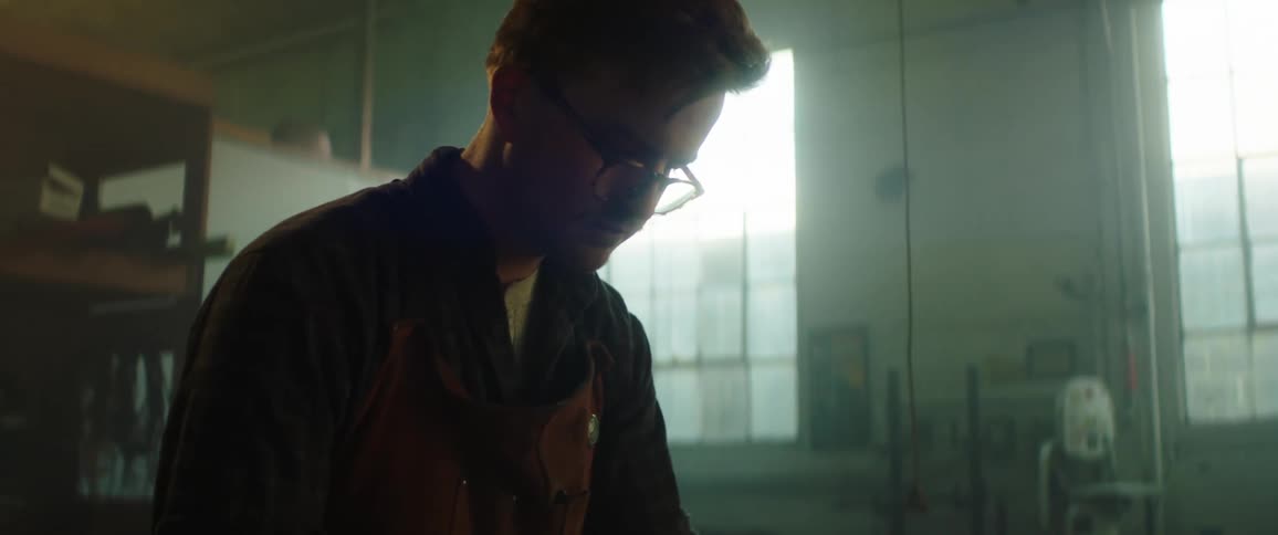 Man crafting the blade of a knife inside a dimly lit workshop