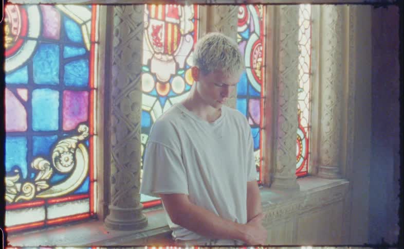 Young man with blood on his face standing in front of stained glass windows inside a church