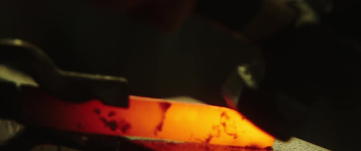 A blacksmith hammering a piece of red hot metal over an anvil inside a dark room