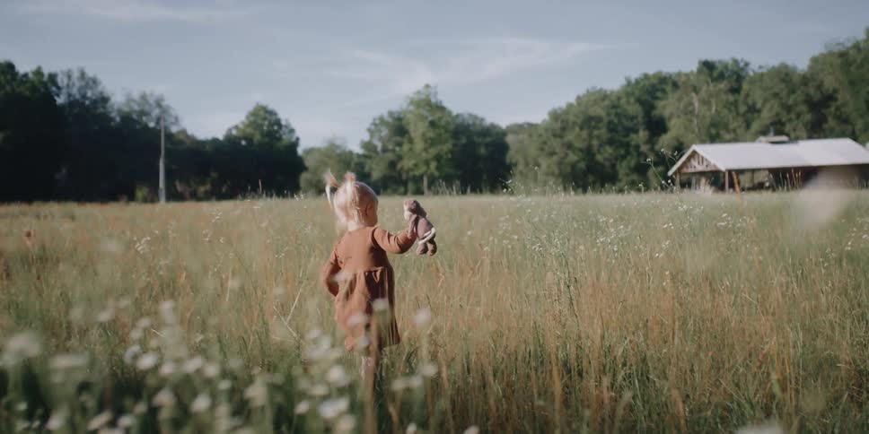 A young child walks through a field of flowers in a rural area