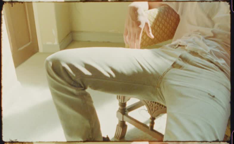 A teenager poses while sitting on an orange patterned chair in combat boots and khakis