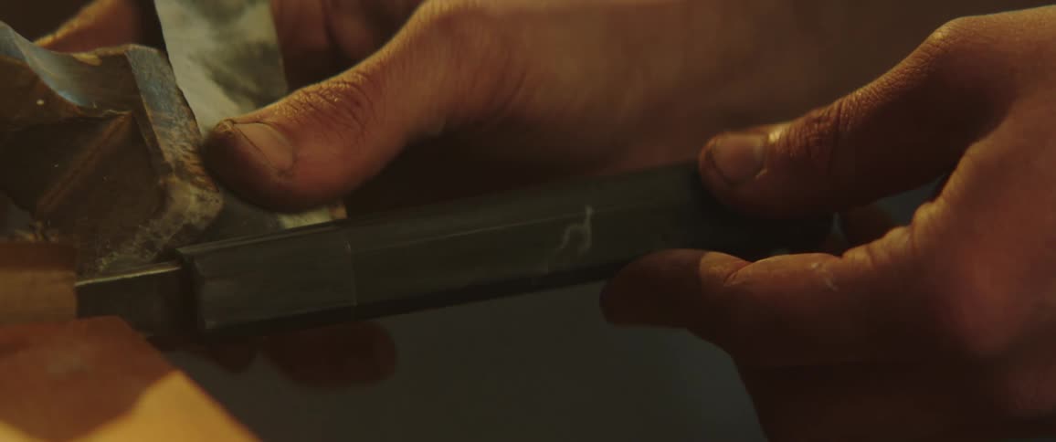 Person runs hand tool along metal piece near workbench