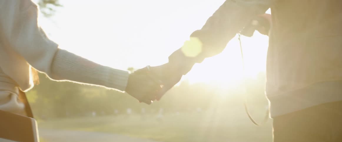 A man and a woman holding hands and walking with trees the sky and clouds in the background
