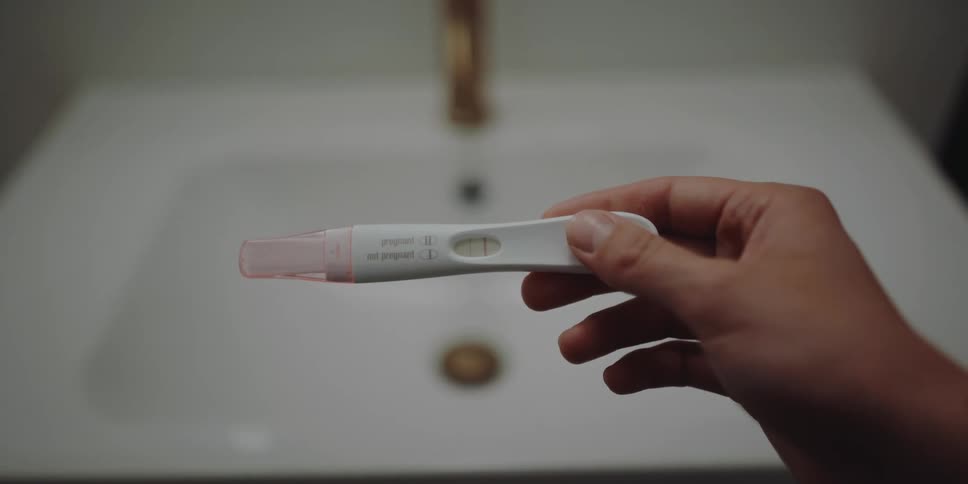 A woman checking a pregnancy test in front of a bathroom sink