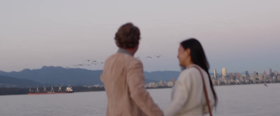 Couple on a date stands in front of a lake while a flock of birds flies overhead