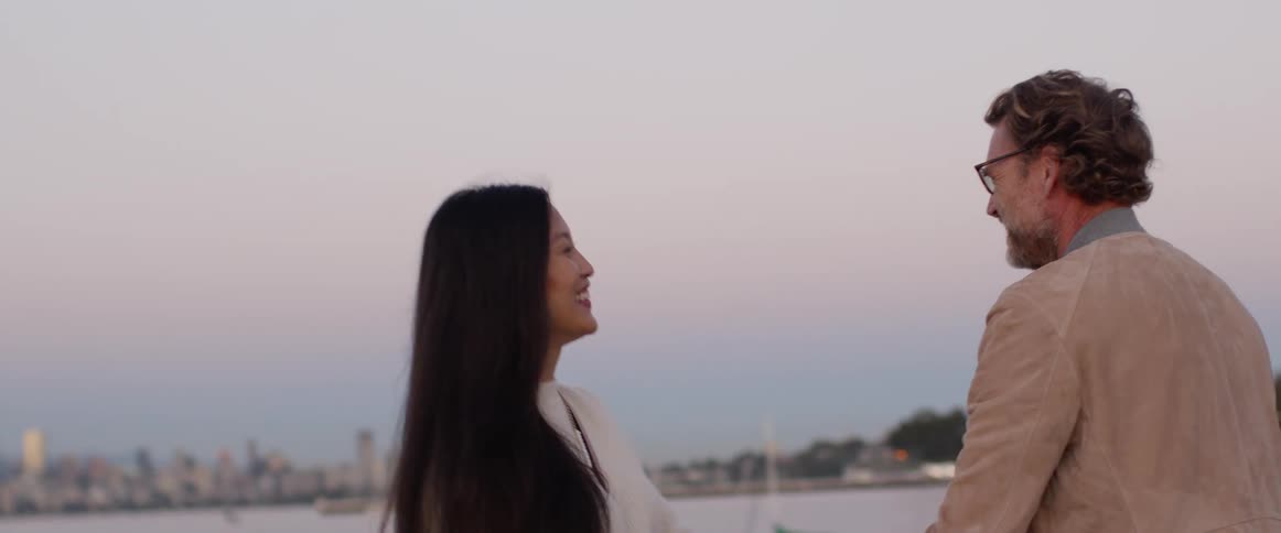 A man and a woman hugging with a body of water the city skyline the sky and clouds in the background