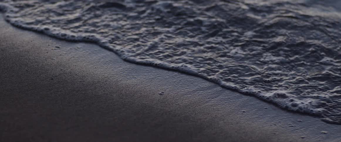 Ocean waves are moving towards the sandy coast at dusk