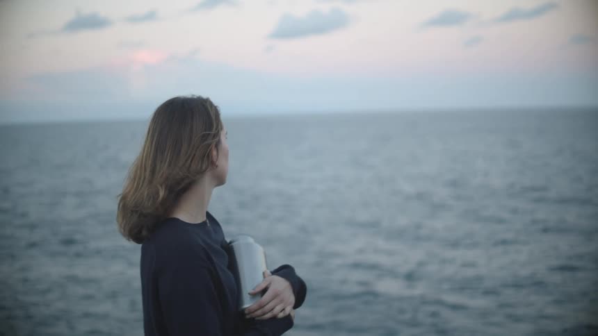 A woman on a beach sprinkling ashes from an urn with the ocean the sky and clouds in the background
