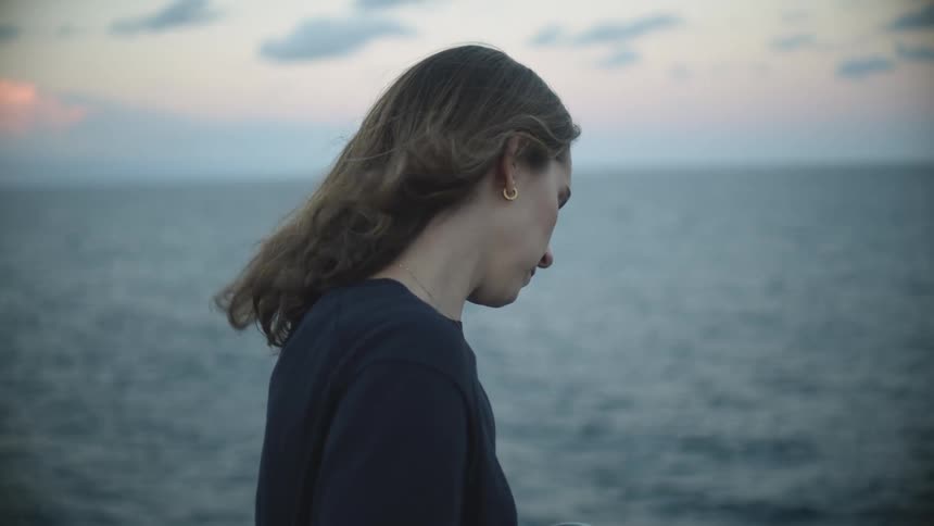 A woman holds an urn closely and kisses the outside of it before spreading the ashes into the ocean