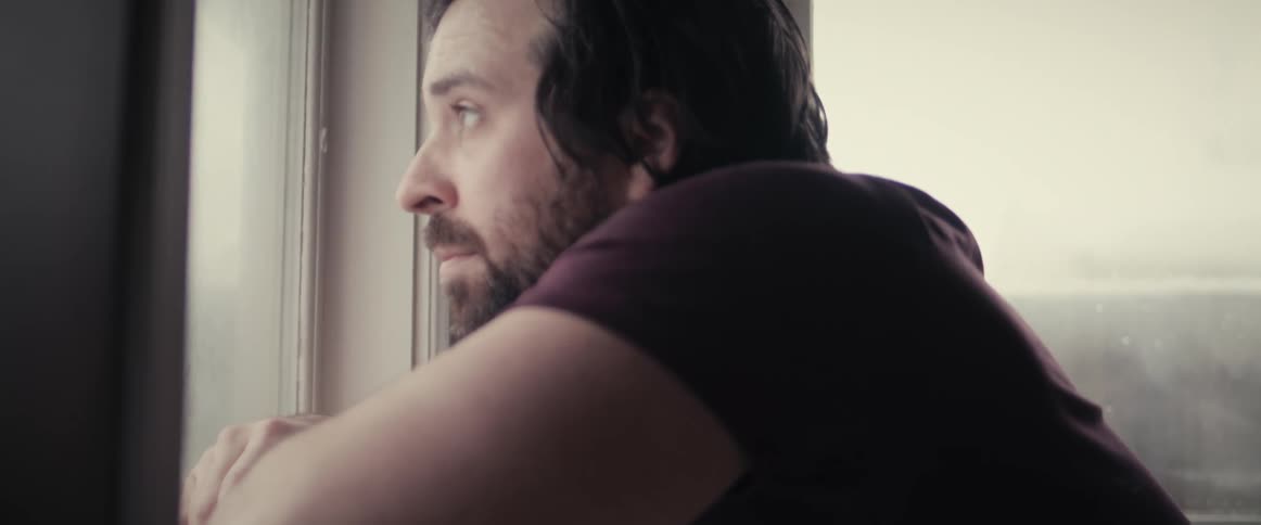 Tired bearded man reclined in the window sill looking outside