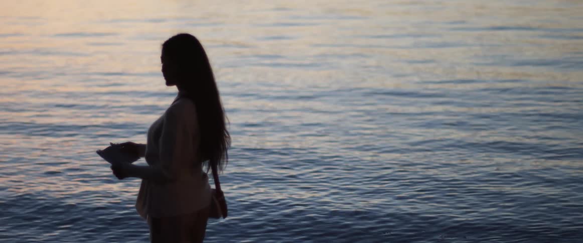 A woman stands and reads a letter next to the ocean