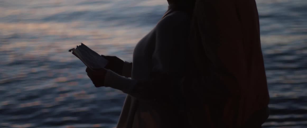 A couple are standing together on the beach at sunset