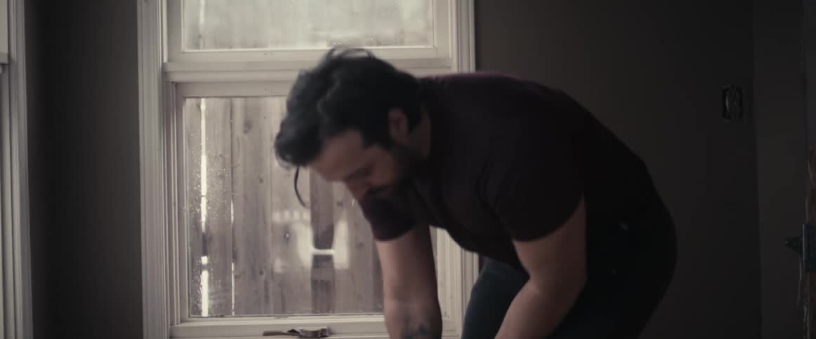 A man in a room working out with a kettlebell with a wall and window in the background