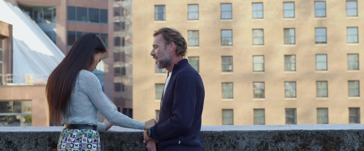 A man and woman stand on a rooftop together holding hands and talking