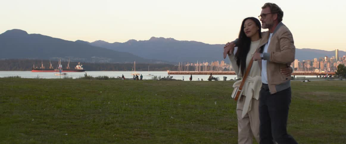 A man wraps his arm around the back of a woman as they walk on a park pathway together