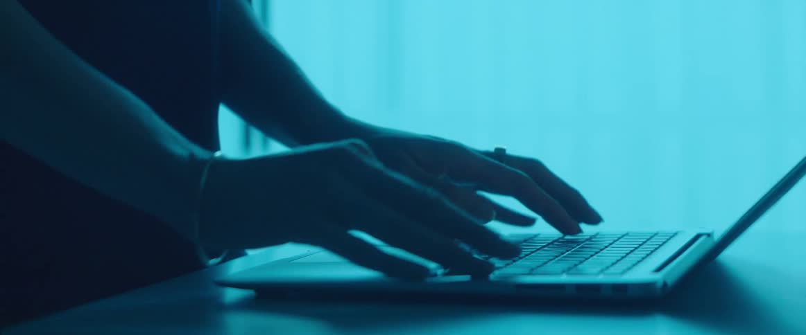 A person typing on the keyboard of a laptop inside a dimly lit room