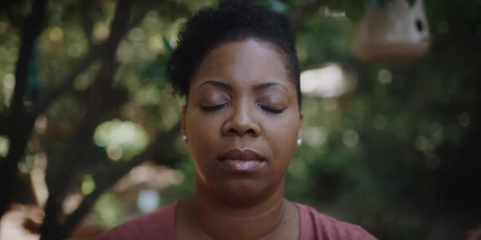 A woman stands still with her eyes closed while positioned beneath a grove of trees