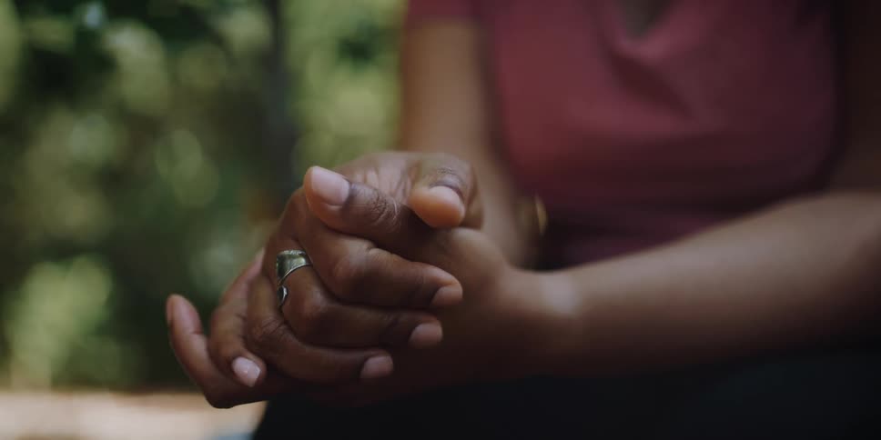 Woman sits with clasped hands outdoors on windy day