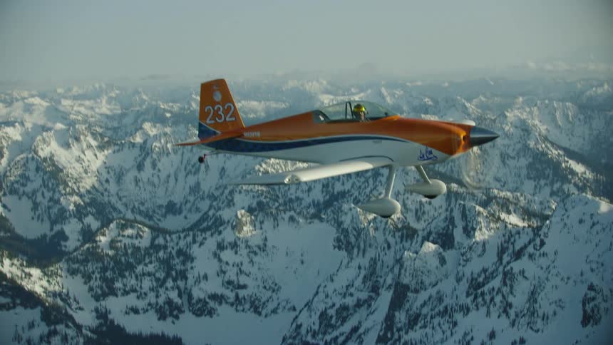 Vivid shot of a single engine orange aircraft flying straight and level over snow covered alpine peaks