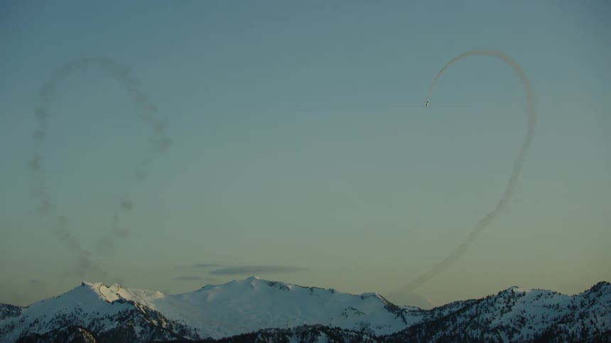 An airplane performs back to back loops in front of snow covered peaks in the high alpine Cascade mountains