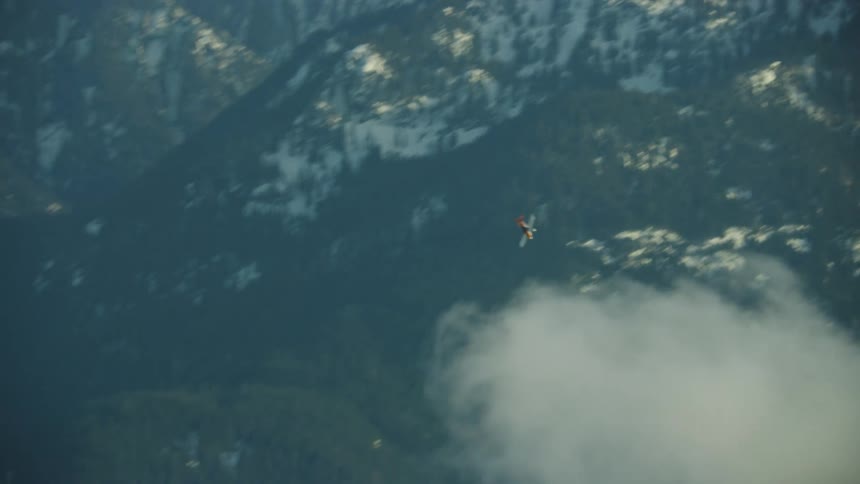 A small passenger airplane dives, climbs and turns quickly in front of huge snow covered mountains