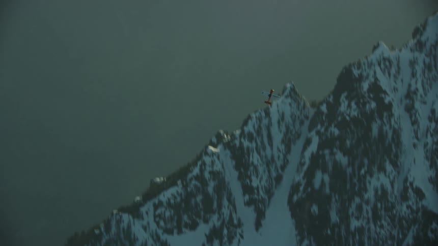 A single engine airplane turns and climbs rapidly in front of golden evening clouds and snow covered peaks in golden light of sunset in winter