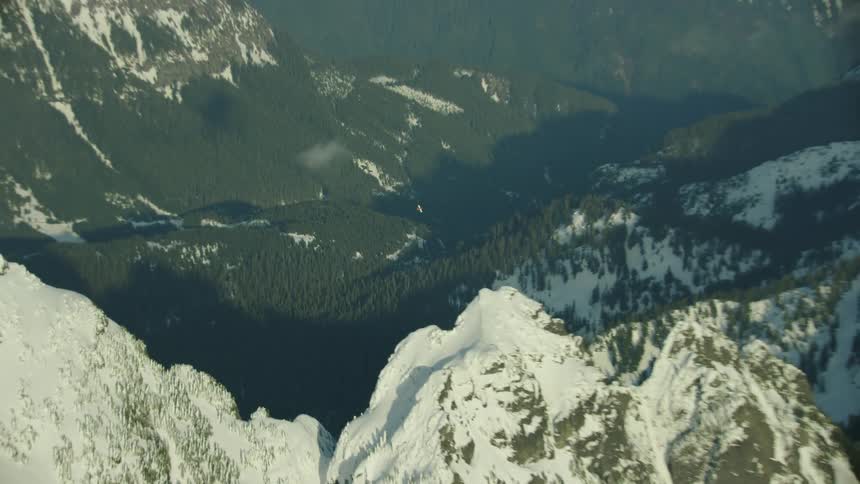 A rapid zoom out reveals a dynamic and vast mountain landscape as the single engine airplane flies center frame in the dramatic mountain winter environment