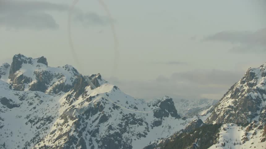 Single engine airplane performs a massive loop in front of awesome alpine mountain peaks in the heart of winter