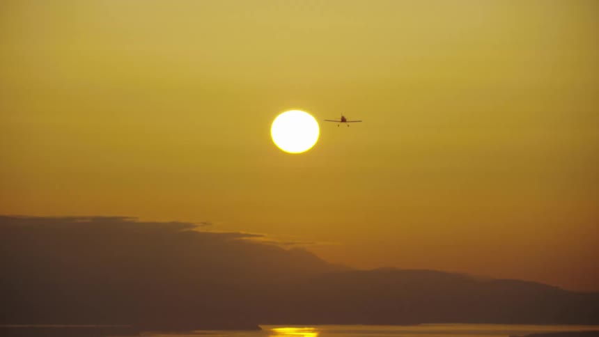 Single engine Vans RV acrobatic airplane flies straight towards the setting sun and Puget Sound at the end of a great day