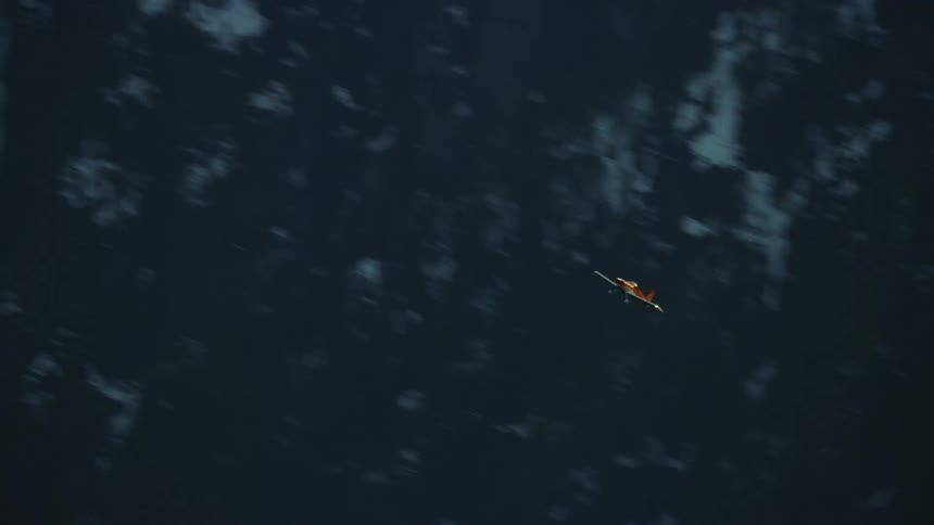 A small single engine airplane flying fast and maneuvering making s turns high above the snow covered mountains