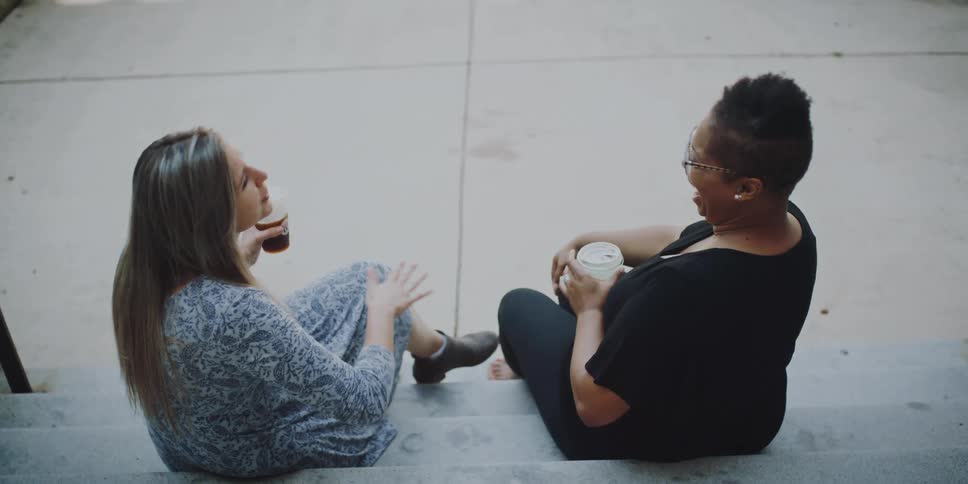 Two woman sit together on some steps outdoors while having a lively conversation