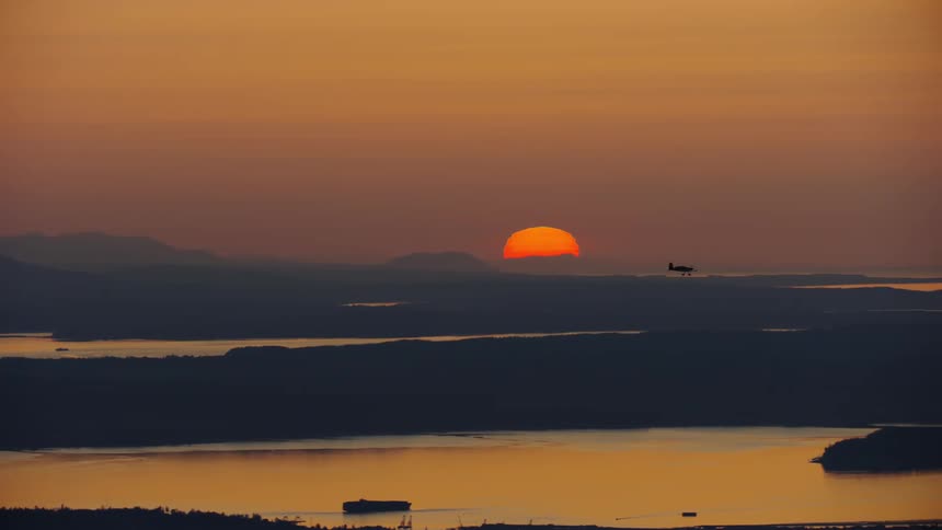 Single engine aircraft flying in front of the setting red sun over the Puget Sound in the Pacific Northwest