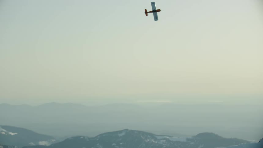 A single engine airplane flies over snow covered mountains before climbing straight up and diving out of frame directly towards the camera - high energy shot